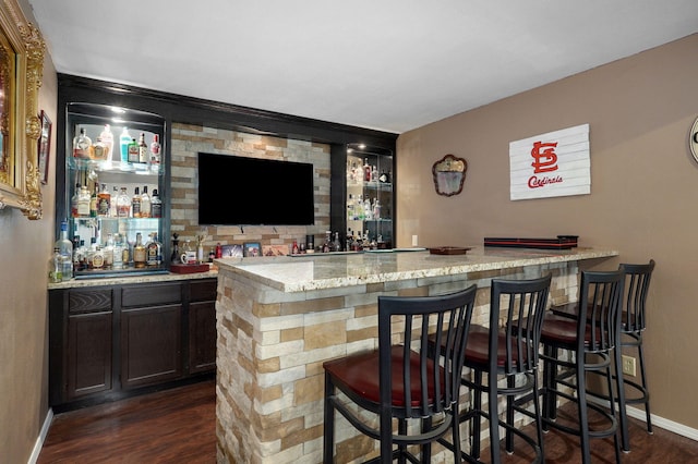 bar featuring light stone counters, dark brown cabinetry, and dark hardwood / wood-style flooring