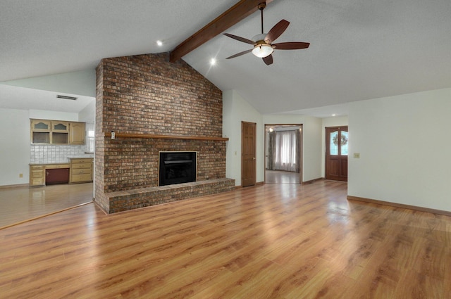 unfurnished living room with a brick fireplace, light hardwood / wood-style floors, lofted ceiling with beams, ceiling fan, and a textured ceiling