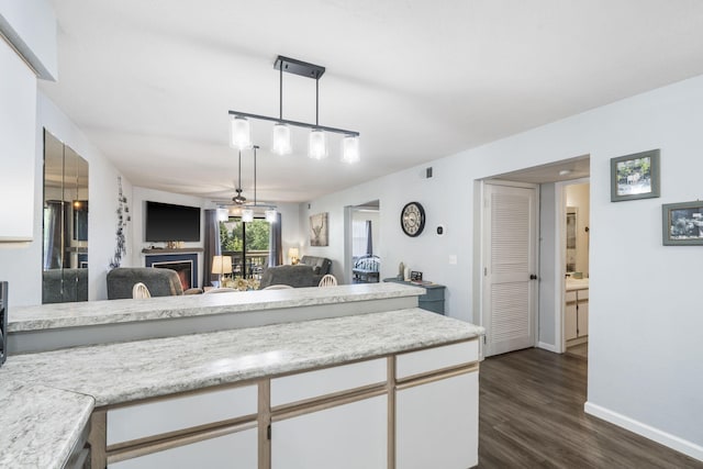 kitchen with light stone counters, ceiling fan, dark wood-type flooring, pendant lighting, and white cabinetry