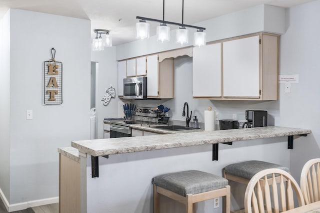 kitchen featuring sink, kitchen peninsula, decorative light fixtures, white cabinetry, and appliances with stainless steel finishes