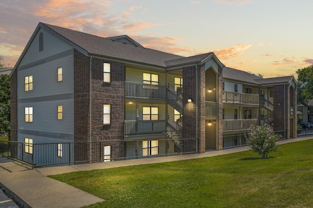 back house at dusk featuring a balcony and a lawn