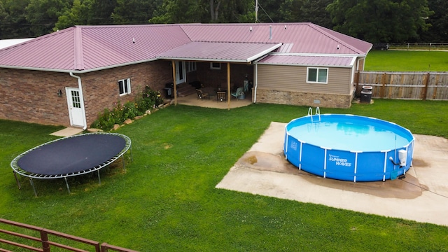 view of pool featuring a lawn, a trampoline, and a patio area