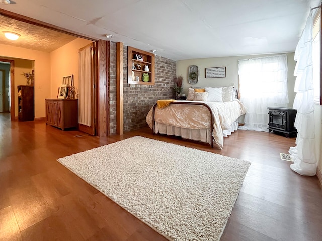 bedroom with brick wall, dark wood-type flooring, and a wood stove