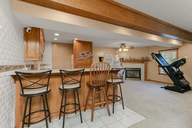 kitchen with ceiling fan, kitchen peninsula, a tiled fireplace, a breakfast bar, and light colored carpet