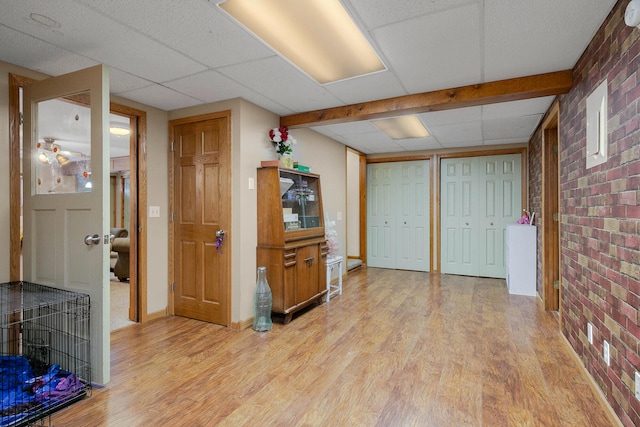 interior space with a paneled ceiling, brick wall, and light hardwood / wood-style flooring