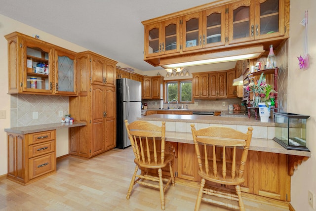 kitchen featuring stainless steel fridge, kitchen peninsula, light hardwood / wood-style flooring, a kitchen breakfast bar, and decorative backsplash