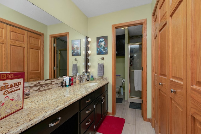 bathroom featuring vanity, tasteful backsplash, tile patterned floors, a shower with shower door, and toilet