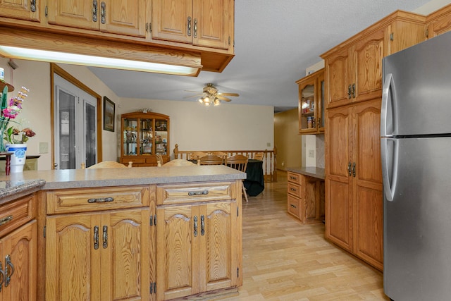 kitchen featuring ceiling fan, stainless steel refrigerator, light hardwood / wood-style floors, kitchen peninsula, and a textured ceiling