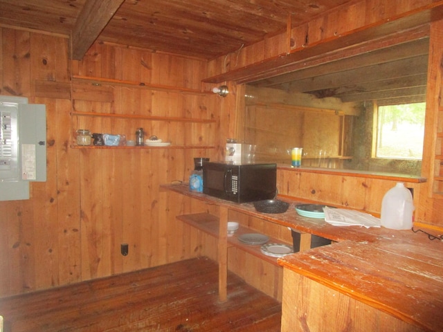 kitchen featuring electric panel, black microwave, wooden walls, and beam ceiling