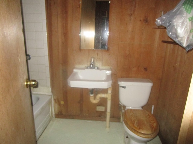 full bathroom with tiled shower / bath, wooden walls, toilet, and sink