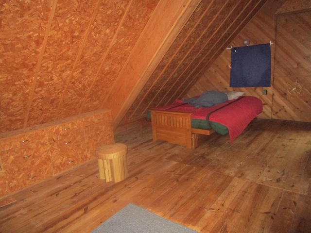 bedroom with vaulted ceiling, wood walls, and wood-type flooring