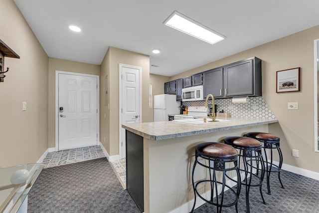 kitchen featuring white appliances, a breakfast bar area, light countertops, backsplash, and a peninsula