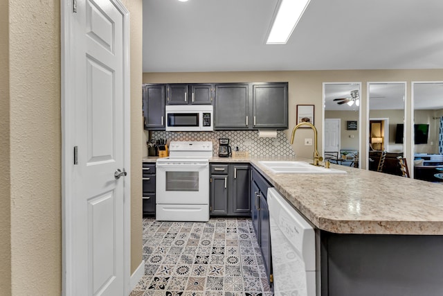 kitchen featuring a peninsula, a sink, tasteful backsplash, white appliances, and light countertops