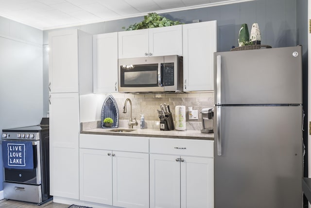 kitchen with a sink, backsplash, white cabinetry, appliances with stainless steel finishes, and ornamental molding