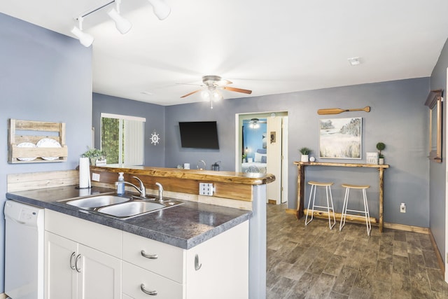 kitchen featuring dark countertops, dishwasher, a sink, a peninsula, and ceiling fan