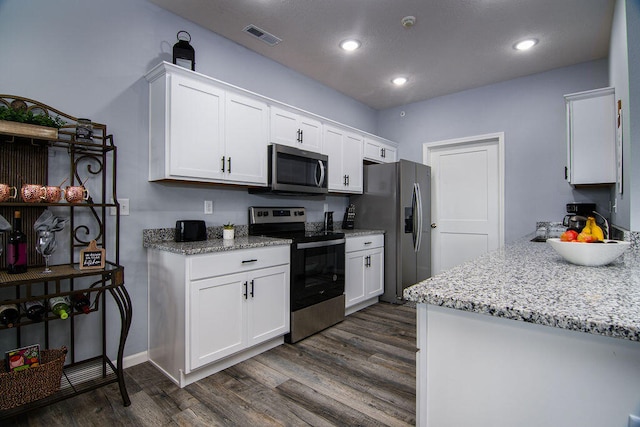 kitchen with light stone countertops, dark hardwood / wood-style floors, white cabinets, and appliances with stainless steel finishes