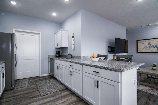 kitchen with white cabinets, appliances with stainless steel finishes, kitchen peninsula, and dark hardwood / wood-style flooring