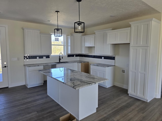 kitchen featuring dark wood-style floors, white cabinetry, a kitchen island, and a sink