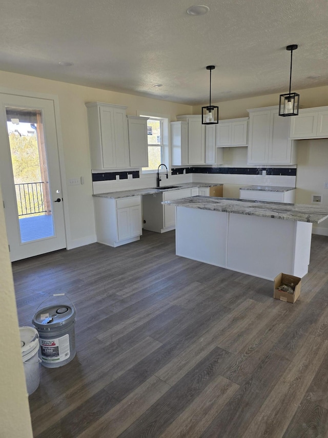 kitchen with a sink, decorative light fixtures, dark wood finished floors, a center island, and white cabinets