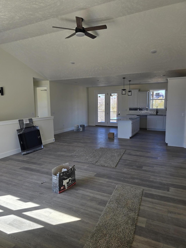 unfurnished living room with dark wood finished floors, lofted ceiling, a healthy amount of sunlight, and baseboards