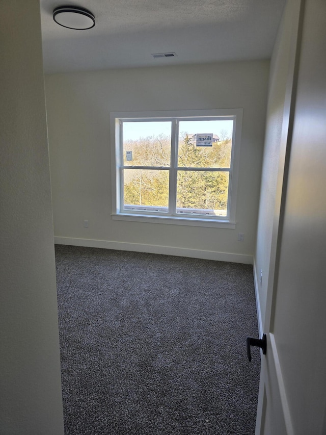 empty room featuring visible vents, baseboards, and dark carpet