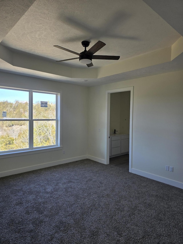 spare room featuring ceiling fan, baseboards, a textured ceiling, a raised ceiling, and dark colored carpet