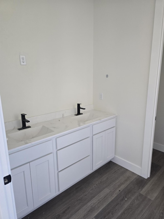 bathroom with double vanity, wood finished floors, baseboards, and a sink