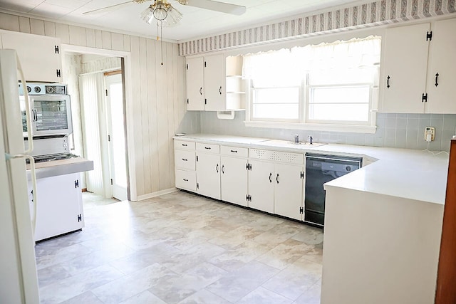 kitchen featuring wooden walls, ceiling fan, white cabinets, and dishwasher