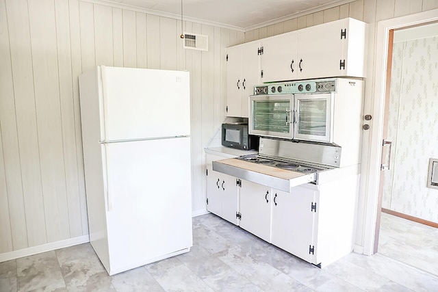 kitchen featuring ornamental molding, wooden walls, white refrigerator, and white cabinets