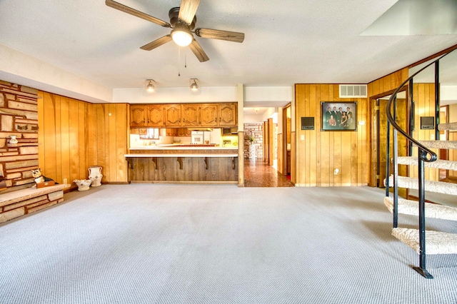 unfurnished living room featuring light colored carpet, ceiling fan, wood walls, and a textured ceiling