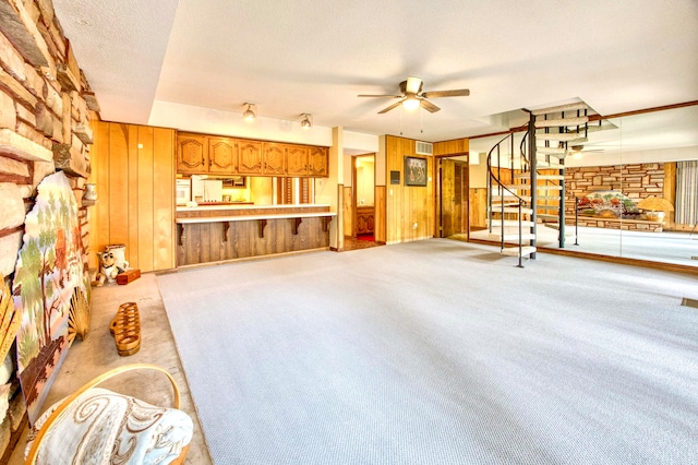 carpeted living room with wood walls, ceiling fan, and a textured ceiling