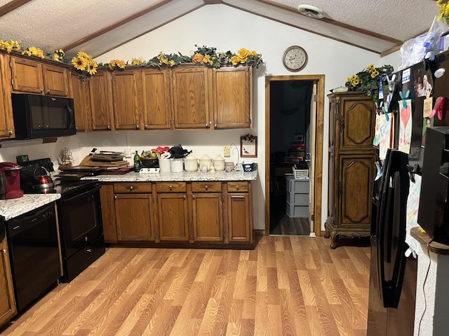 kitchen featuring vaulted ceiling, a textured ceiling, black appliances, brown cabinets, and light wood finished floors