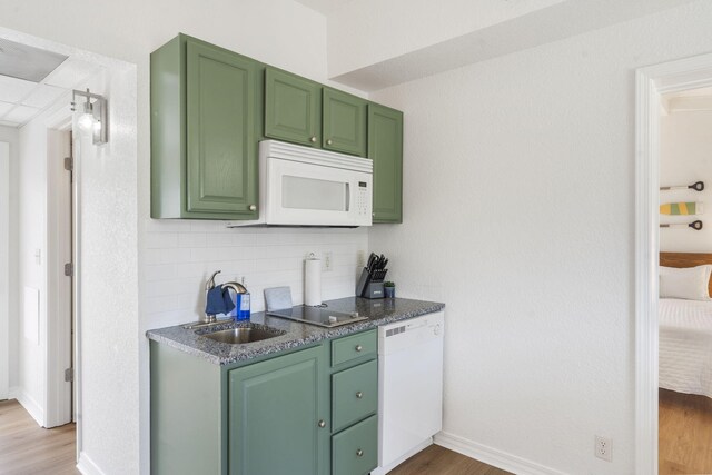 kitchen featuring white appliances, light wood-style flooring, a sink, green cabinets, and backsplash