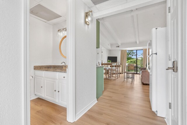 hallway featuring lofted ceiling with beams, baseboards, light wood-type flooring, and a sink