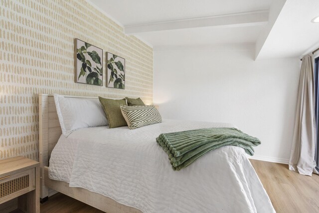 bedroom featuring beam ceiling, wallpapered walls, baseboards, and wood finished floors