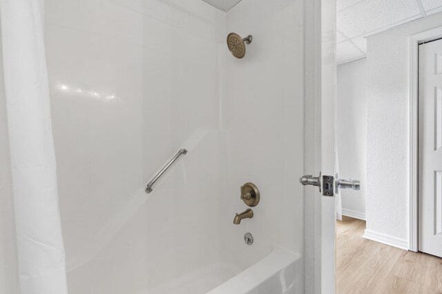 bathroom featuring tub / shower combination, a drop ceiling, baseboards, and wood finished floors