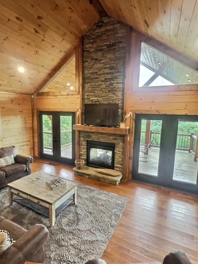 living room with hardwood / wood-style floors, french doors, wood ceiling, a stone fireplace, and wood walls