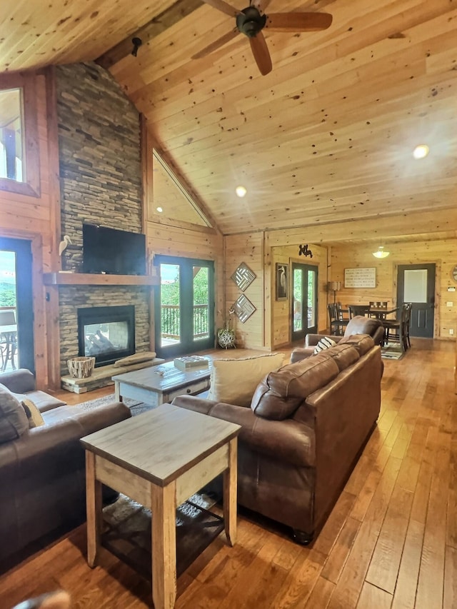 living room with a stone fireplace, light wood-type flooring, high vaulted ceiling, and a wealth of natural light