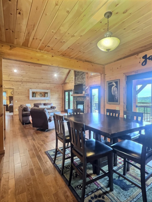 dining room with hardwood / wood-style floors, a wealth of natural light, a stone fireplace, and vaulted ceiling