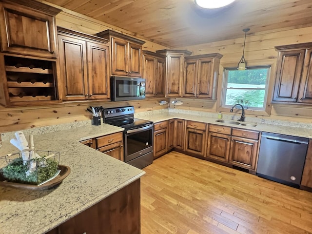 kitchen featuring sink, hanging light fixtures, light hardwood / wood-style flooring, appliances with stainless steel finishes, and wood walls