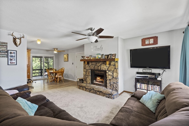 living area featuring lofted ceiling, ceiling fan, a stone fireplace, and baseboards