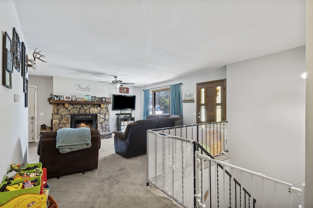 carpeted living room with ceiling fan and a stone fireplace