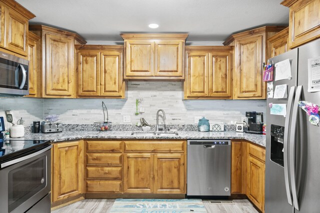 kitchen with stainless steel appliances, a sink, decorative backsplash, and light stone countertops