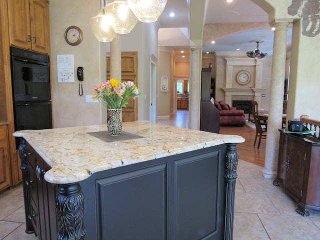 kitchen with light stone counters, black double oven, decorative columns, and a kitchen island