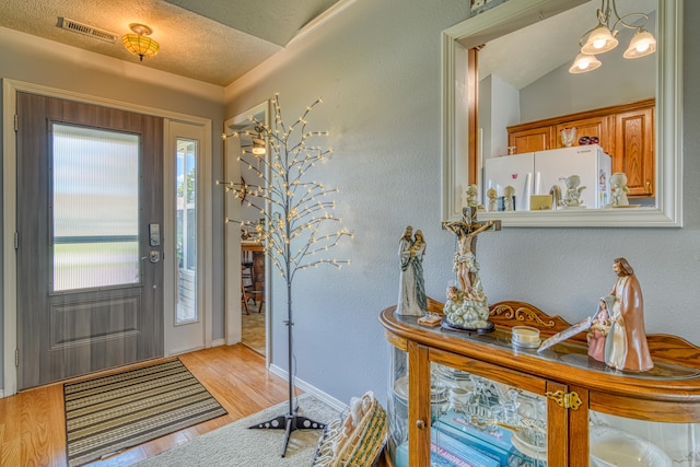 entryway featuring lofted ceiling, light hardwood / wood-style floors, and a textured ceiling