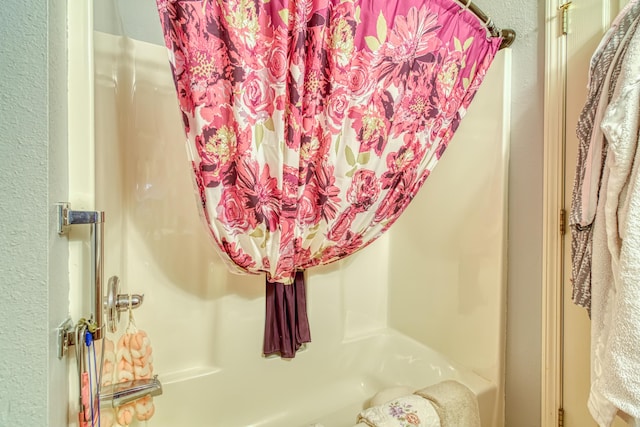 details with shower / tub combo and a textured wall