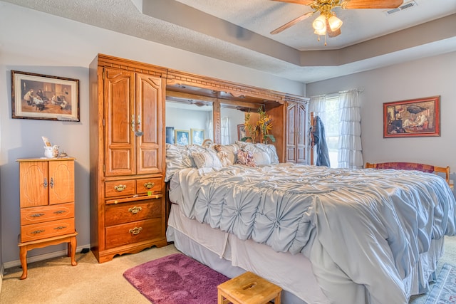 bedroom with a tray ceiling, light colored carpet, a textured ceiling, and ceiling fan