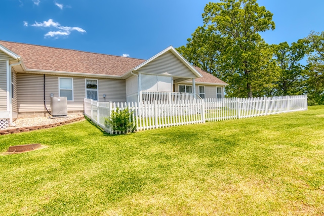 back of property with cooling unit, a yard, a shingled roof, and fence