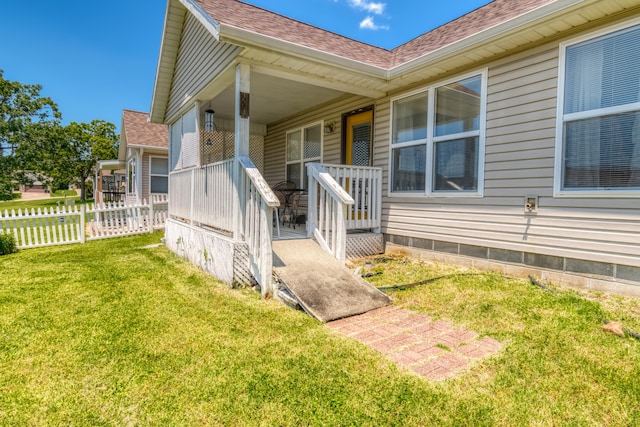 view of exterior entry with a lawn, a shingled roof, covered porch, and fence