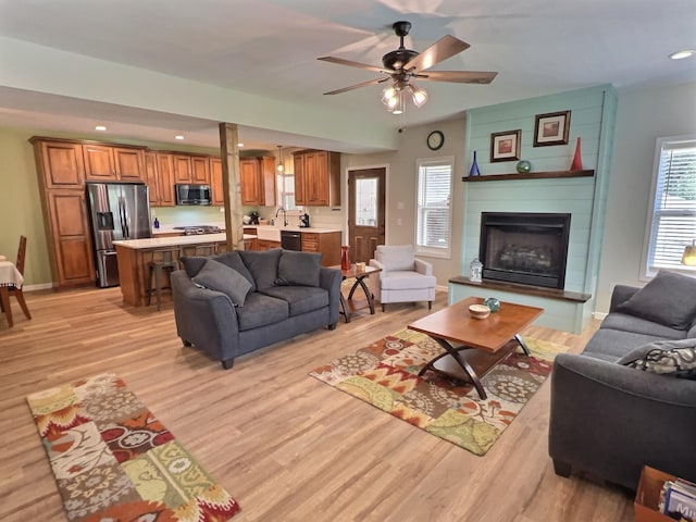 living room with ceiling fan, light hardwood / wood-style flooring, a fireplace, and sink